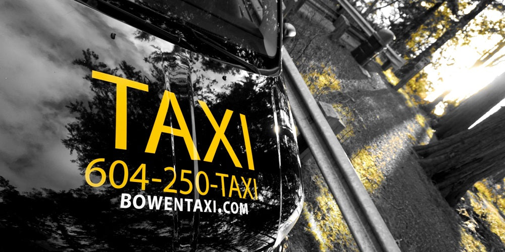 Front hood of the Bowen land taxi displays the phone number and website is seen parked near a grove of sunny trees.